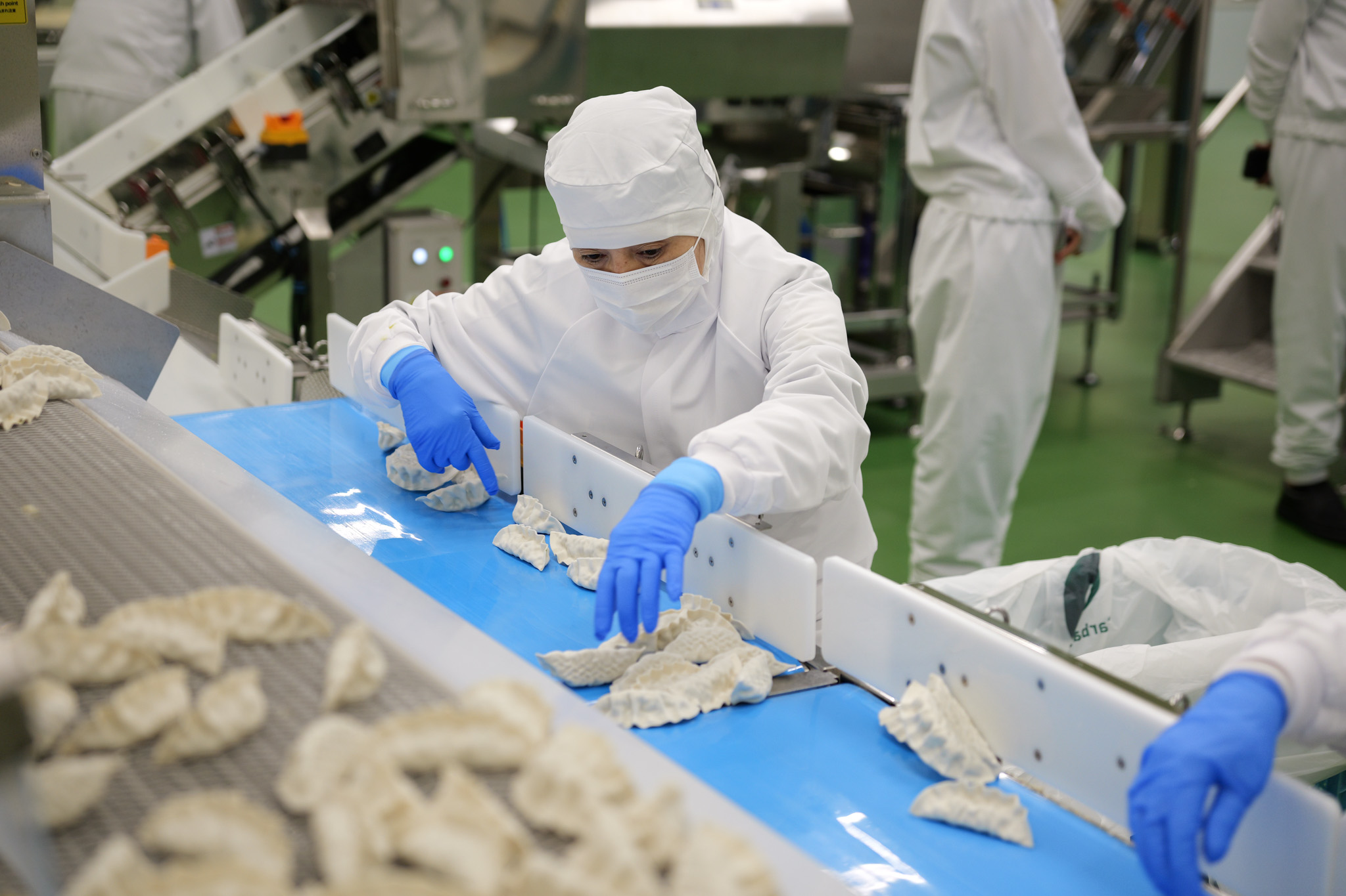 A masked worker in a white uniform sorts through bibigo Mandu in the Chiba facility.