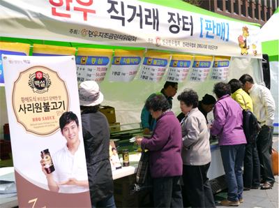 청계천 한우 직거래 장터에 한 부스가 보인다. 백설 사리워 불고기 양념 시식을 하고 있으며 어르신 6분이 부스 앞에 서서 시식과 구경을 하고 계신다.