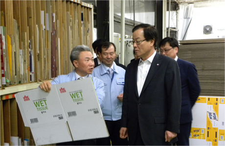 포장재가 가득 든 공장 안에서 포장재 협력사 대표가 CJ제일제당 대표이사 김철하에게 자사 제품을 설명 하고 있다. 뒤에는 남자 4명이 서있다.